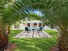 Backyard featuring a paved stone patio with pebble accents, a swimming pool, mature palm trees, and a covered terrace supported by columns