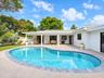 Covered patio with architectural columns, stone-paver pool deck, and freeform swimming pool featuring a decorative stone border
