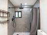 Shower area featuring large-format grey tile walls, a white hexagonal tile floor, matte black rainfall showerhead with handheld sprayer, and built-in 