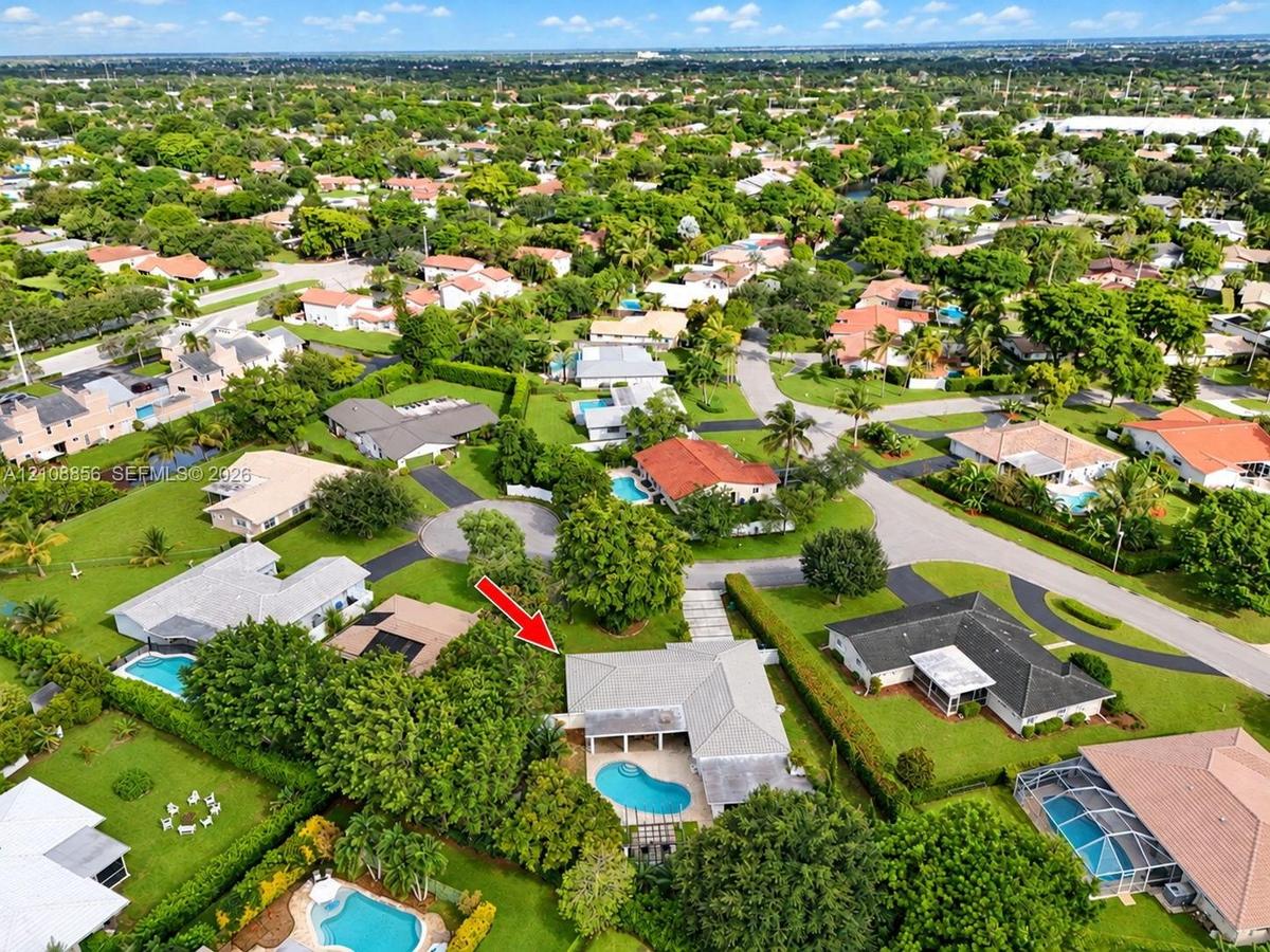 Aerial perspective of a single-story residence featuring a private swimming pool, concrete patio, hipped roofline, and mature landscaping