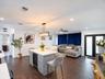 Open-concept living space featuring wood-finish flooring, recessed lighting, a central kitchen island with integrated wine refrigeration and stone-fin