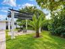 Outdoor living area featuring a pergola supported by classic columns, stone paver patio, manicured lawn, and mature landscaping