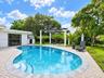 Custom-shaped swimming pool with tiered entry steps, herringbone-patterned stone paver patio, and pergola supported by white columns