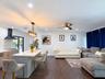 Open-concept kitchen and living area featuring a center island with light-toned solid surface countertop, white brick backsplash, matte black range ho