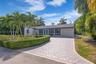 Single-story residence featuring a paved patterned driveway, attached garage, stone-accented facade, and manicured hedge landscaping with mature palm 