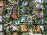 Aerial perspective of a property featuring an in-ground swimming pool, concrete patio, paved driveway, and mature landscaping