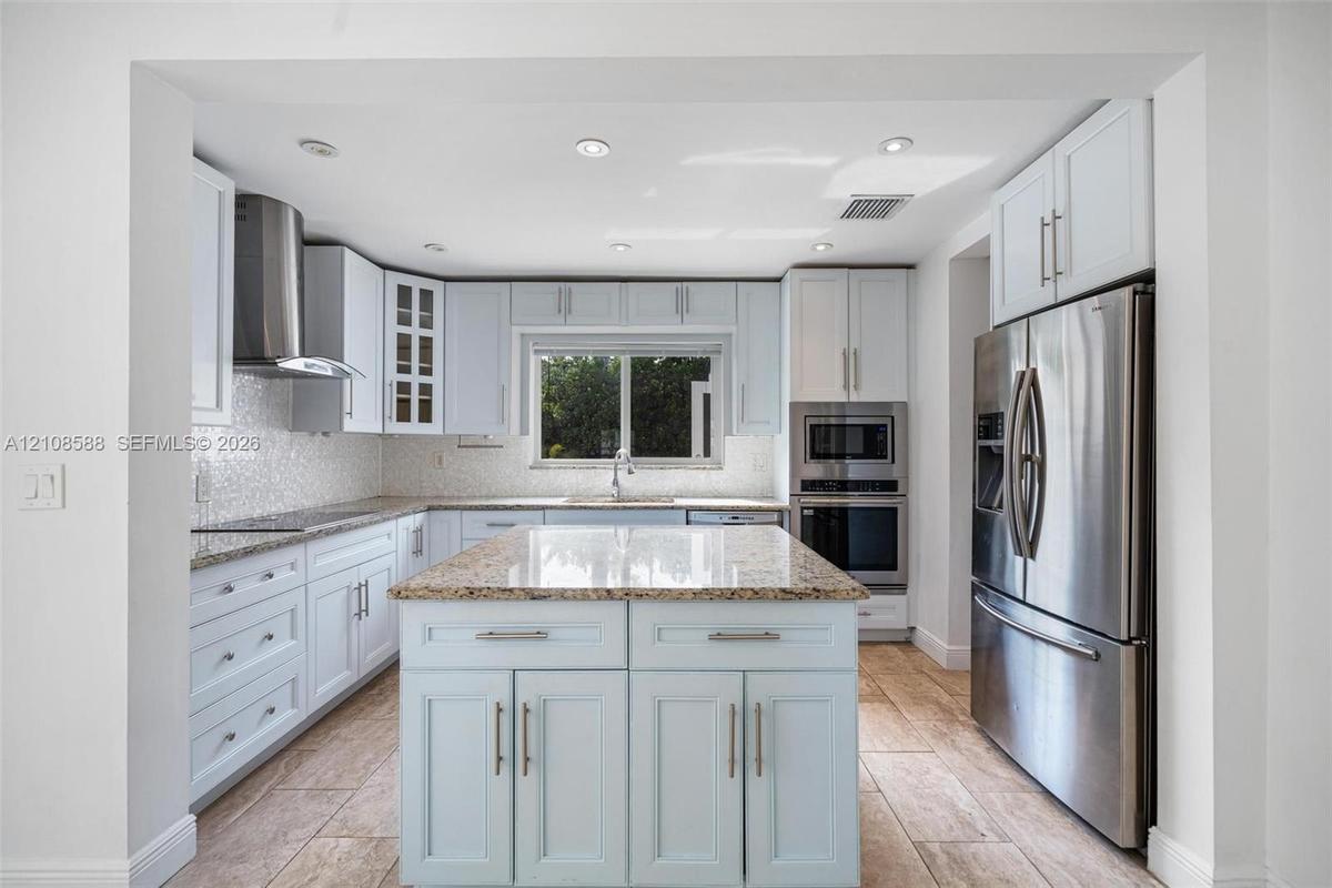 Kitchen featuring white shaker cabinetry, central island with stone countertop, stainless steel appliances, mosaic tile backsplash, and ceramic tile f