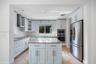 Kitchen featuring white shaker cabinetry, central island with stone countertop, stainless steel appliances, mosaic tile backsplash, and ceramic tile f