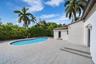 Expansive outdoor patio featuring light-toned concrete pavers, a kidney-shaped in-ground pool, and mature palm trees