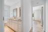 Dual-sink vanity with white cabinetry, stone-finish countertop, and rectangular vessel sinks, complemented by wood-finish flooring in the hallway