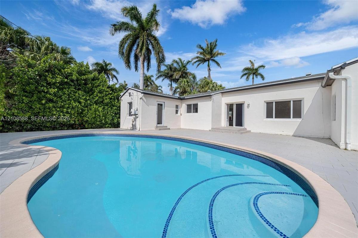 Curved swimming pool featuring built-in steps and a surrounding paved patio