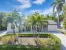 Single-story residence featuring a paved driveway, exterior stone veneer accents, multi-pane windows, attached garage, and mature landscaping with pal