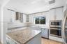 Kitchen featuring white cabinetry, stone countertops, stainless steel appliances including a built-in oven and microwave, mosaic tile backsplash, and 