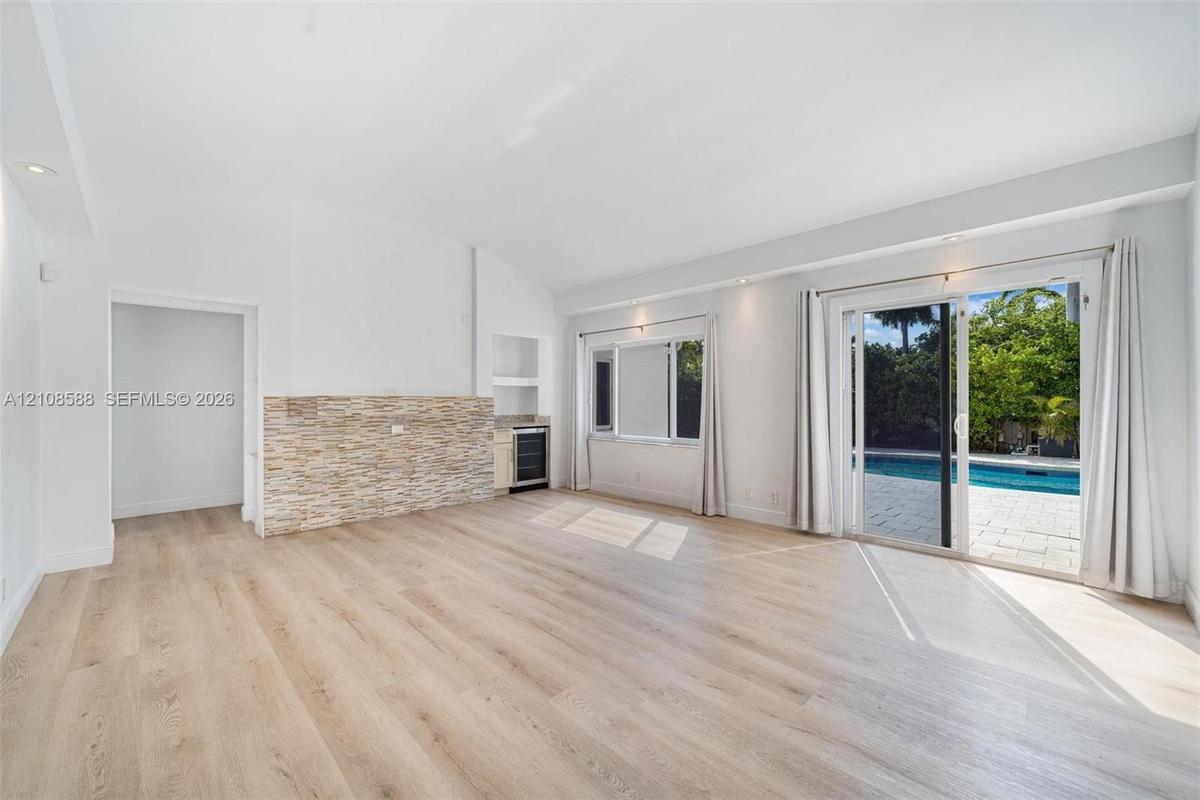 Open-concept interior featuring light wood-finish flooring, vaulted ceilings, a stacked stone accent wall, a built-in beverage refrigerator, and slidi