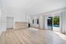 Open-concept interior featuring light wood-finish flooring, vaulted ceilings, a stacked stone accent wall, a built-in beverage refrigerator, and slidi