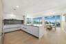 Contemporary kitchen featuring white handleless cabinetry, a substantial quartz-topped center island with integrated sink, stainless steel range hood,