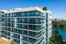 Modern multi-story building featuring white stucco facade, expansive floor-to-ceiling windows, wrap-around glass-railed balconies, and a rooftop terra