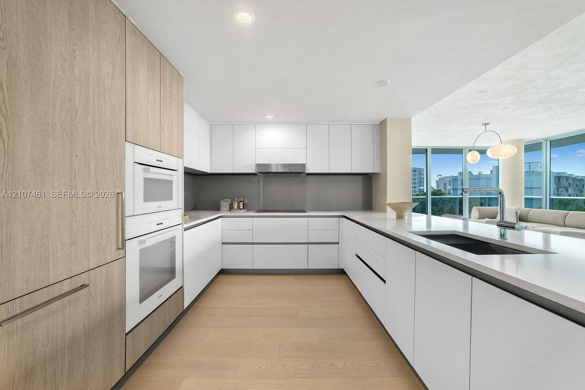 Modern kitchen featuring flat-panel cabinetry, light-toned wood-finish flooring, integrated wall ovens, solid-surface countertops, and recessed lighti