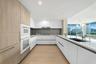 Modern kitchen featuring flat-panel cabinetry, light-toned wood-finish flooring, integrated wall ovens, solid-surface countertops, and recessed lighti