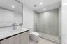 Bathroom featuring a wood-finish vanity with a stone countertop, an integrated rectangular sink, a wall-to-wall mirror, and a walk-in shower with a gl