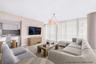 Open-concept living space featuring wood-finish flooring, floor-to-ceiling windows, a modern multi-arm pendant light, and a peninsula kitchen with fla