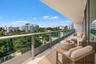 Covered balcony featuring a sleek glass-panel railing, overhead lighting, and expansive urban scenery