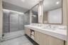 Floating dual vanity with integrated countertop, walk-in shower featuring glass enclosure and stone-tile surrounds, and rectangular wall-mounted mirro