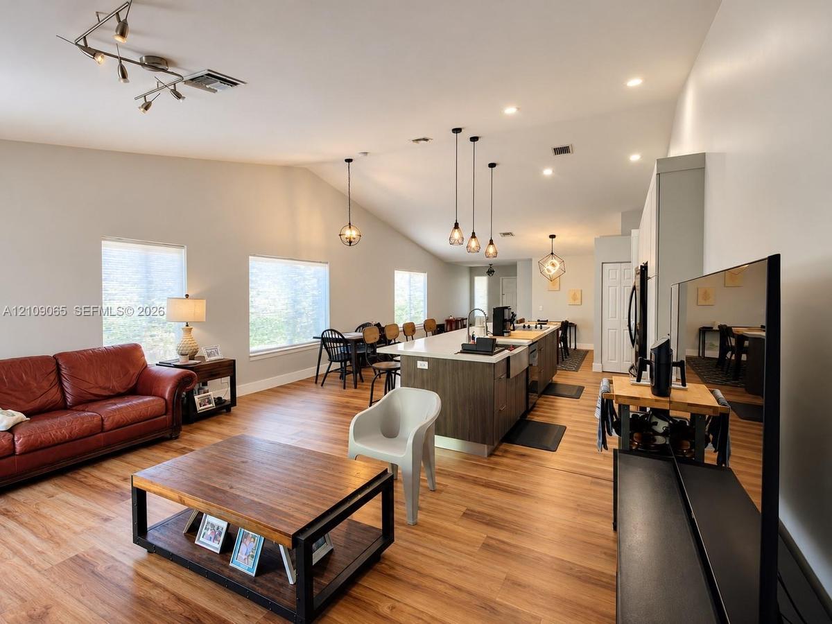 Open-concept space featuring wood-finish flooring, vaulted ceilings, a kitchen island with stone-finish countertops, apron-front sink, and pendant lig