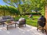 Rear patio featuring large-format light-toned stone tile flooring, horizontal wood-slat privacy fencing, and a grassy lawn bordered by mature trees an