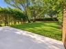 Expansive backyard featuring a smooth-finish paved patio, a sprawling lawn, and mature tree-lined perimeter with established hedges