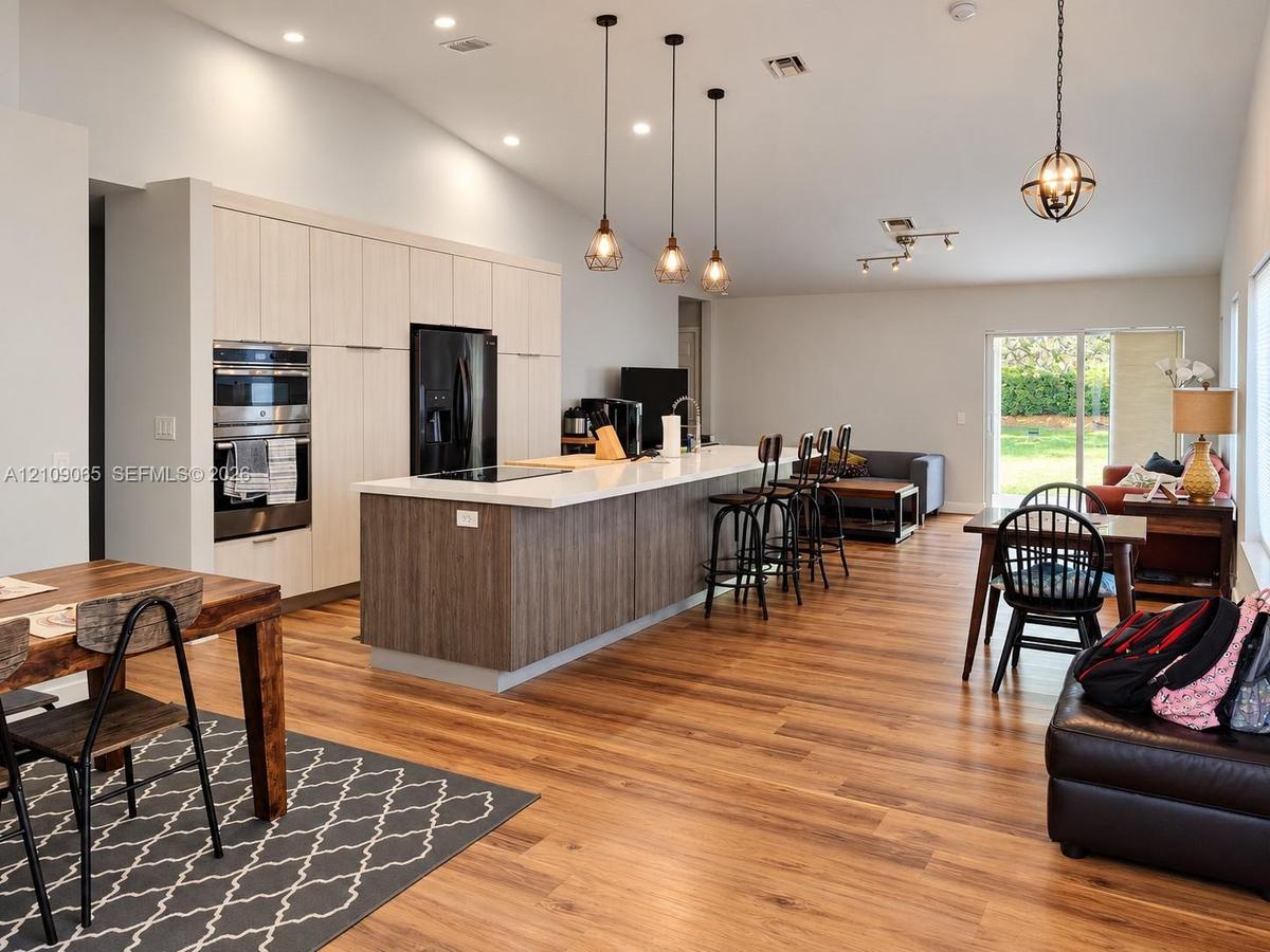 Open-concept kitchen featuring full-height light wood-finish cabinetry, a large center island with contrasting wood-finish paneling and quartz counter