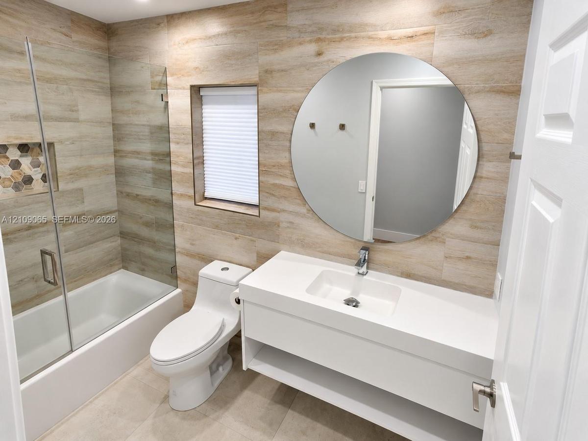 Full-wall wood-finish tile cladding, floating vanity with integrated rectangular basin, frameless glass shower enclosure featuring a built-in recessed
