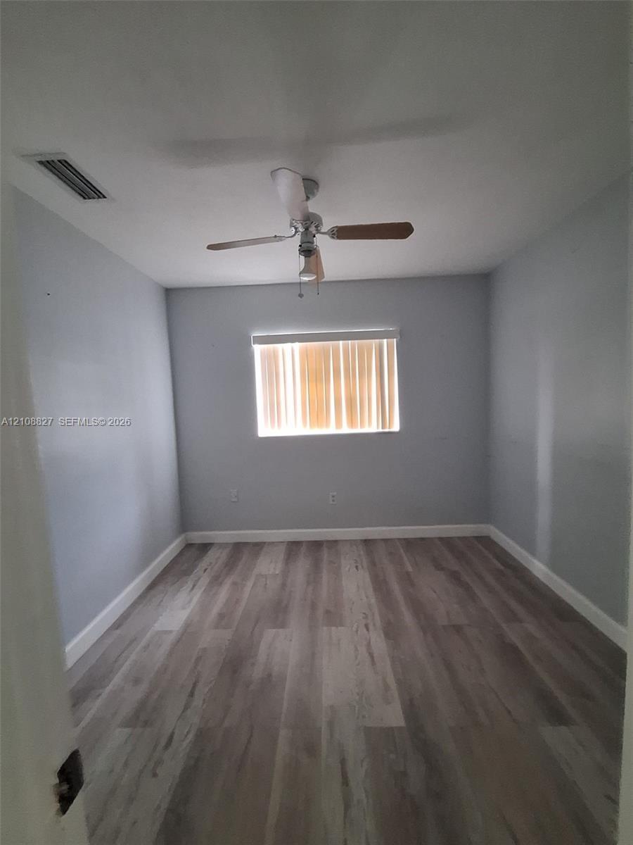 Room featuring wood-finish flooring, a neutral paint palette, and a ceiling-mounted fan with integrated lighting