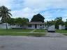 Single-story residence featuring a gray stucco exterior, concrete walkway, paved driveway, and perimeter fencing