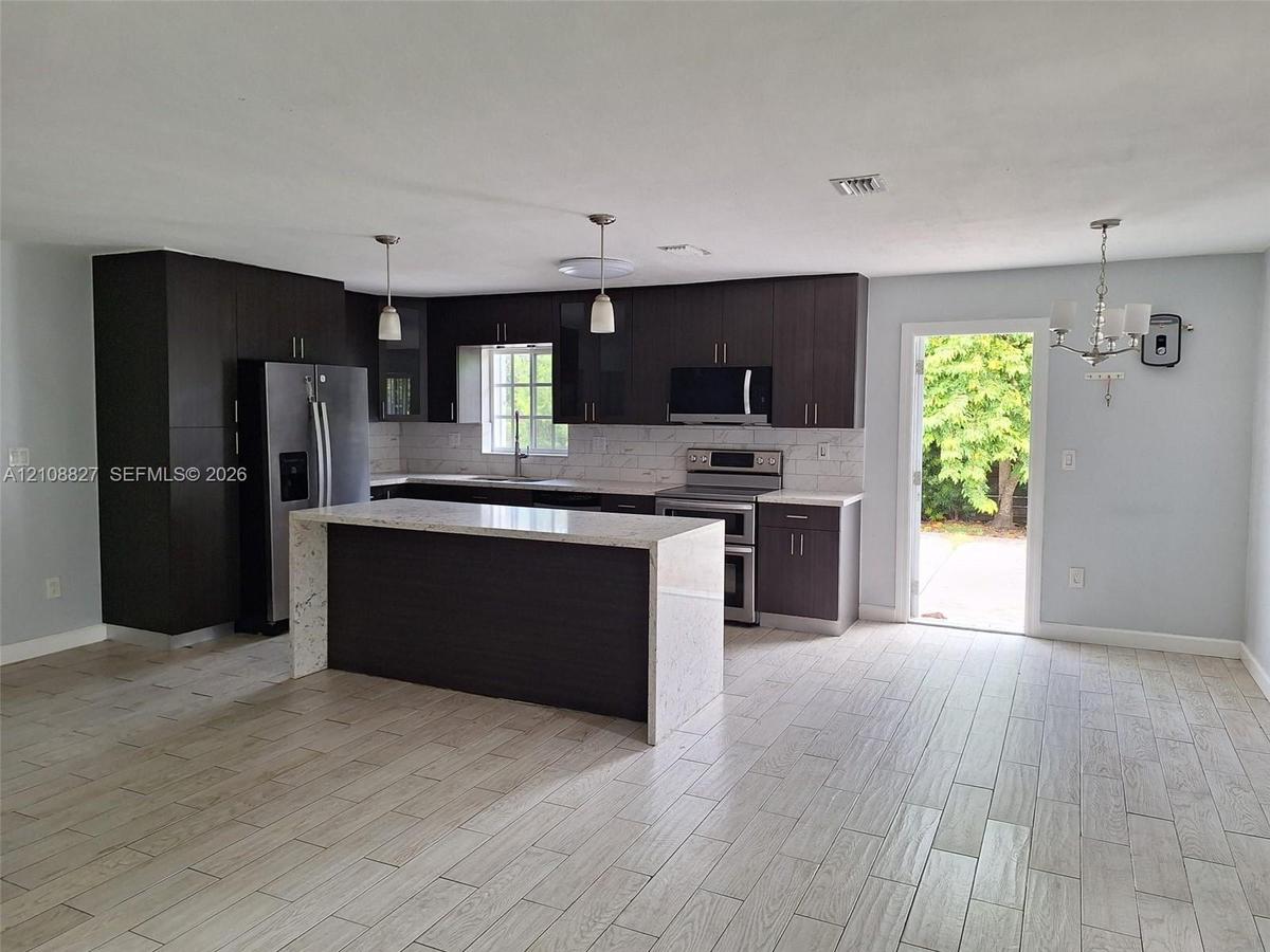 Kitchen featuring dark cabinetry, a waterfall-edge stone island, stainless steel appliances, and wood-finish flooring