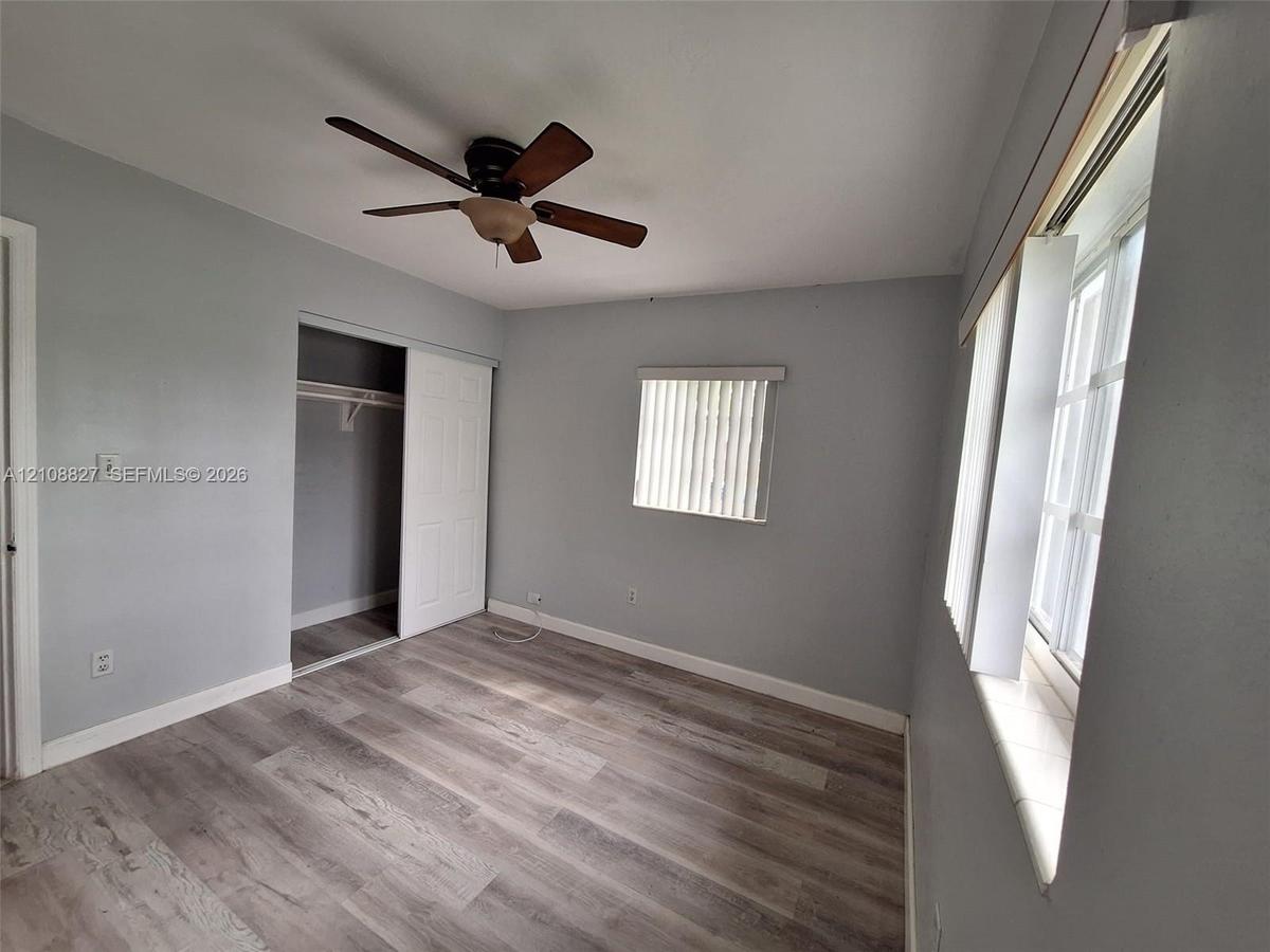 Neutral-toned interior featuring wood-finish flooring, a ceiling fan with integrated lighting, and a closet with a sliding panel door