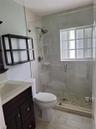 Bathroom featuring a glass-enclosed shower with a pebble stone floor, wood-finish flooring, a dark wood vanity with a solid-surface countertop, and a 