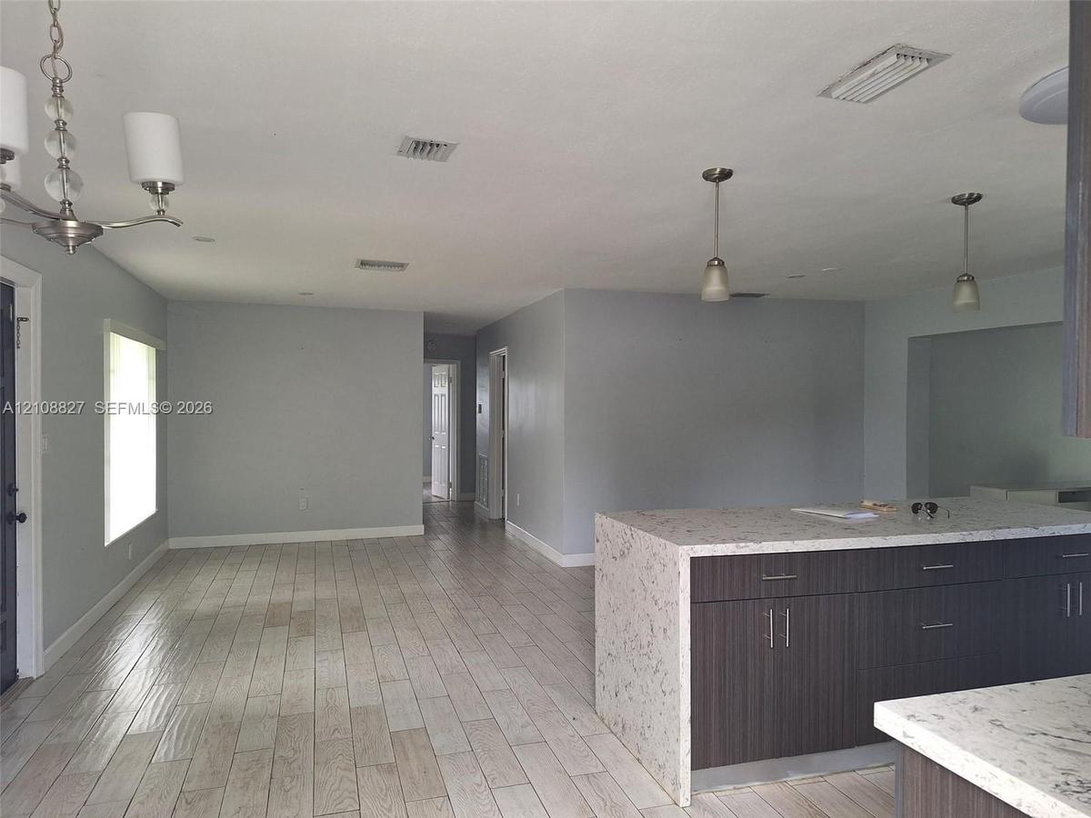 Kitchen featuring a central island with a stone-composite countertop, dark wood-finish cabinetry, neutral wall paint, wood-finish flooring, and pendan