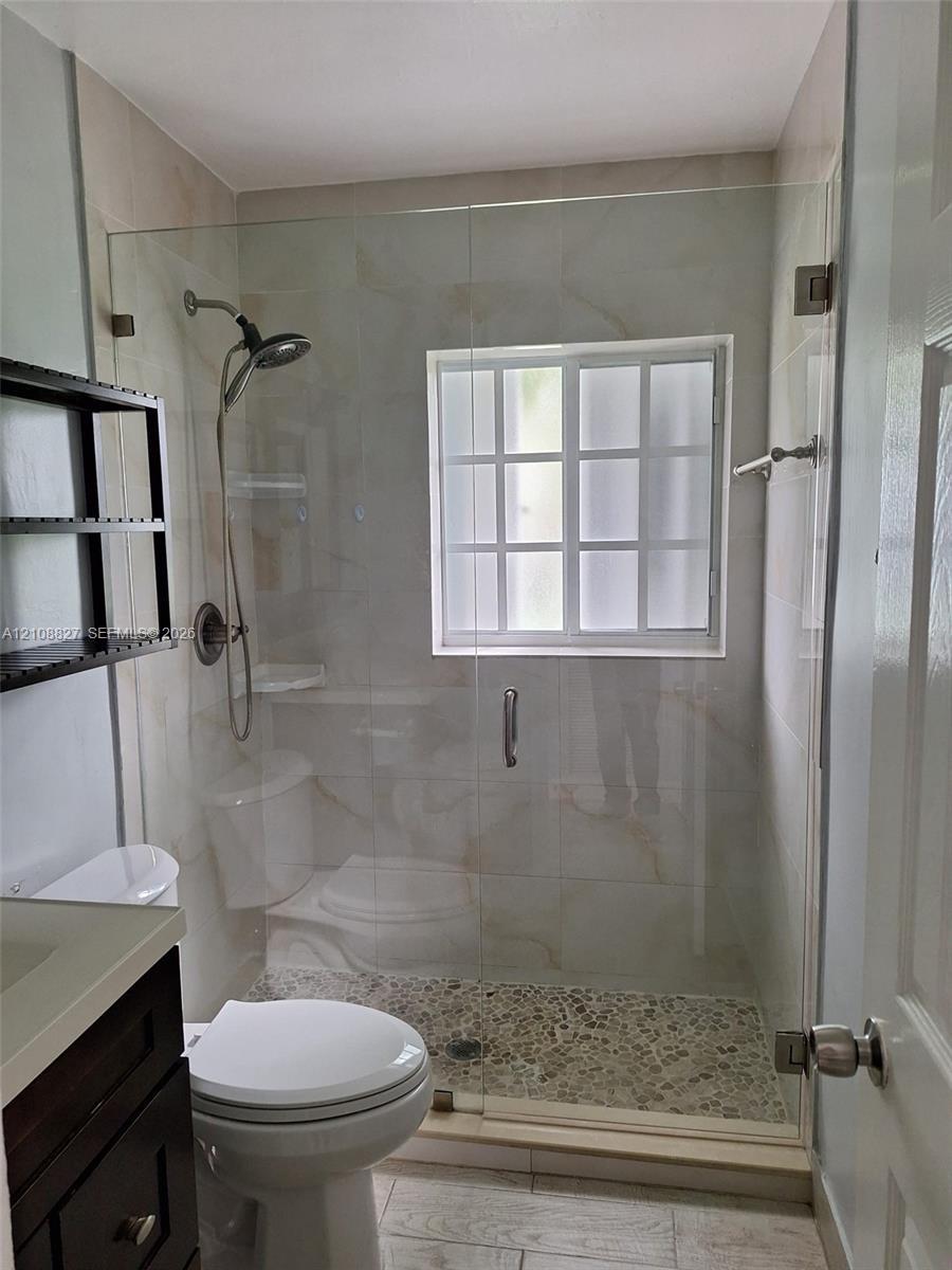 Walk-in shower featuring a frameless glass enclosure, pebble tile flooring, oversized wall tile, and a multi-function showerhead, complemented by a da