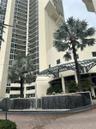 High-rise exterior featuring curved glass balconies, a circular fountain with tiered stone masonry, a metal-framed porte-cochere, and mature palm land