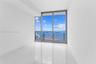 Floor-to-ceiling windows with sliding glass door access to a balcony, polished white stone-finish flooring, and expansive water scenery