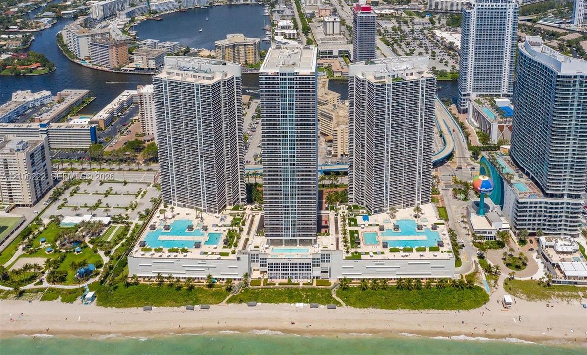 Aerial perspective of oceanfront high-rise residential complex featuring multiple swimming pools, spacious sun decks, extensive podium-level hardscapi