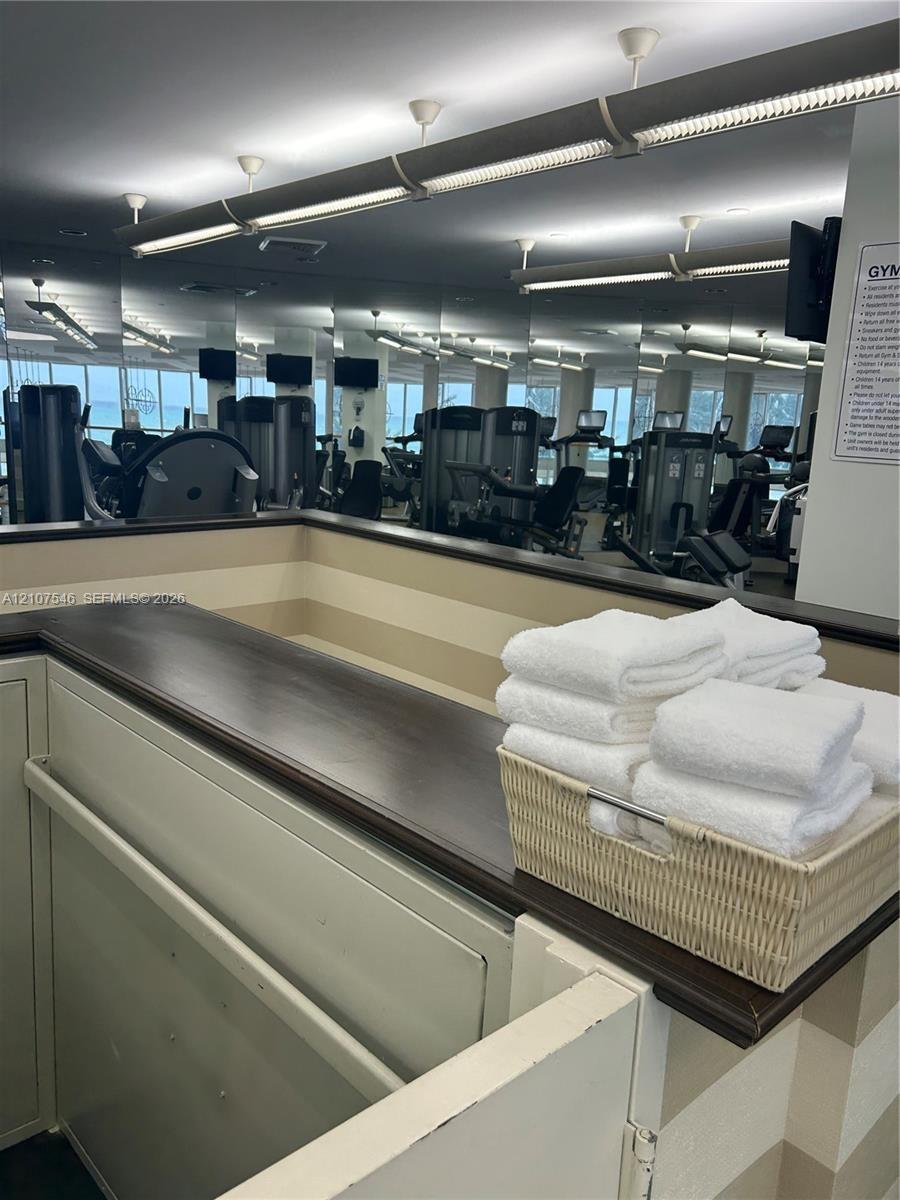 Fitness area featuring full-wall mirrors, recessed lighting, and a built-in service counter with a dark wood-finish top