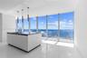 Kitchen island with a dark countertop and integrated sink, complemented by three modern pendant lights and floor-to-ceiling windows featuring coastal 