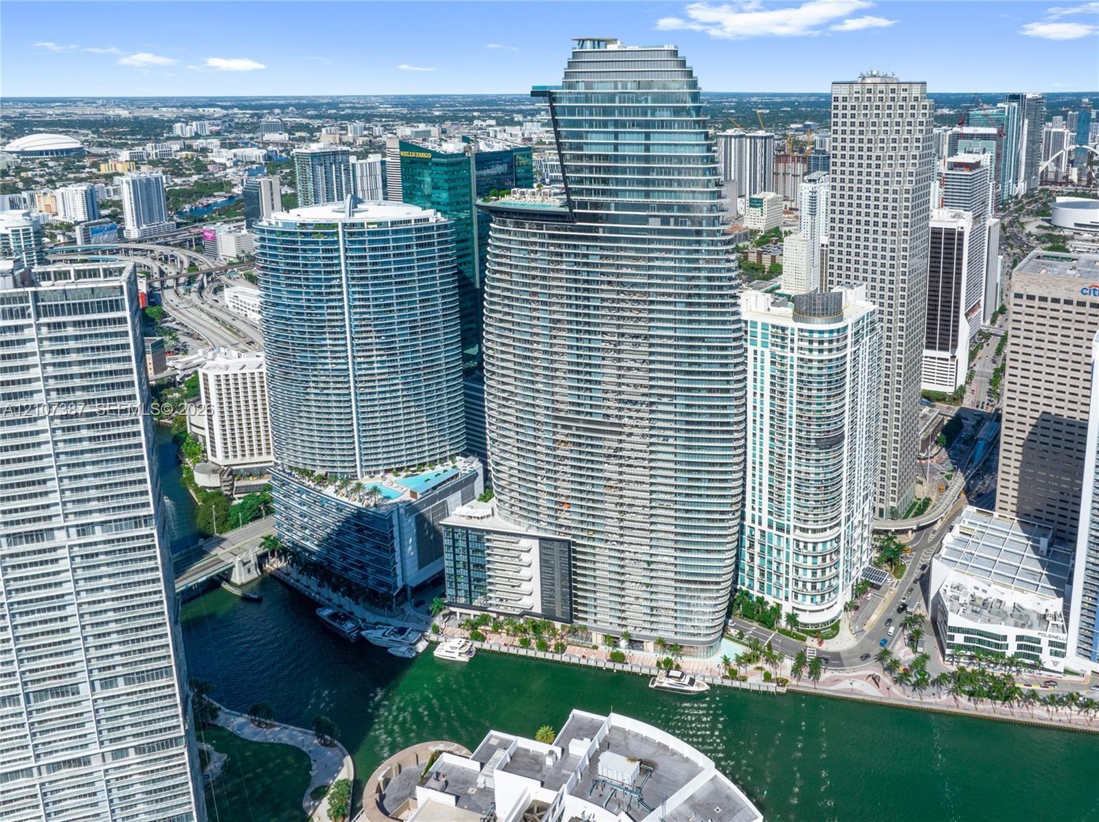 High-rise residential tower featuring a glass-curtain facade, prominent tiered architectural design, and water frontage along a canal