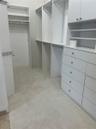 Walk-in closet featuring white built-in cabinetry, floor-to-ceiling shelving, multiple drawer units, and hanging rods