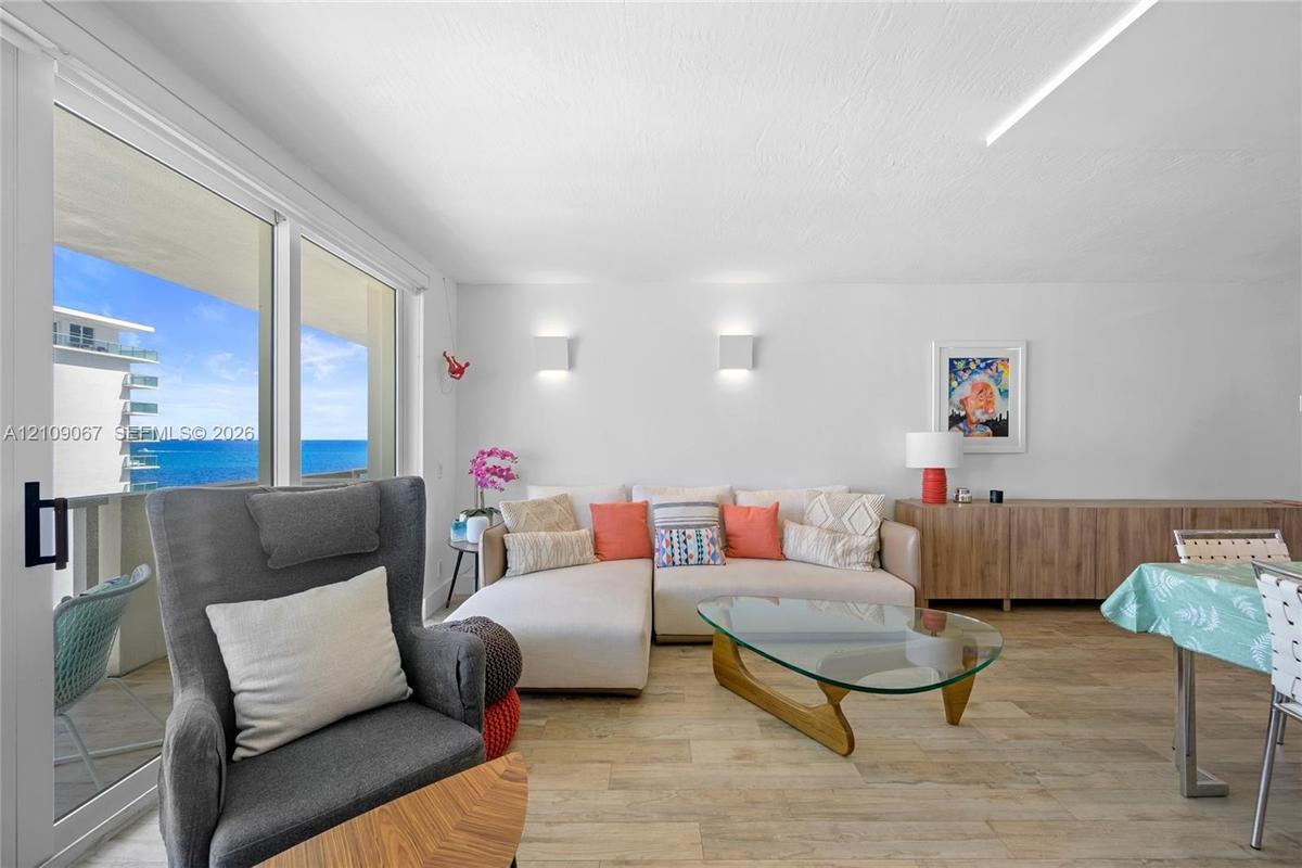 Living area featuring wood-finish flooring, floor-to-ceiling sliding glass doors, wall-mounted light fixtures, and expansive ocean and coastal scenery