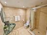 Full-height stone tile wall finishes with matching floor tiling, glass pedestal sink, frameless glass-enclosed shower, and recessed ceiling lighting