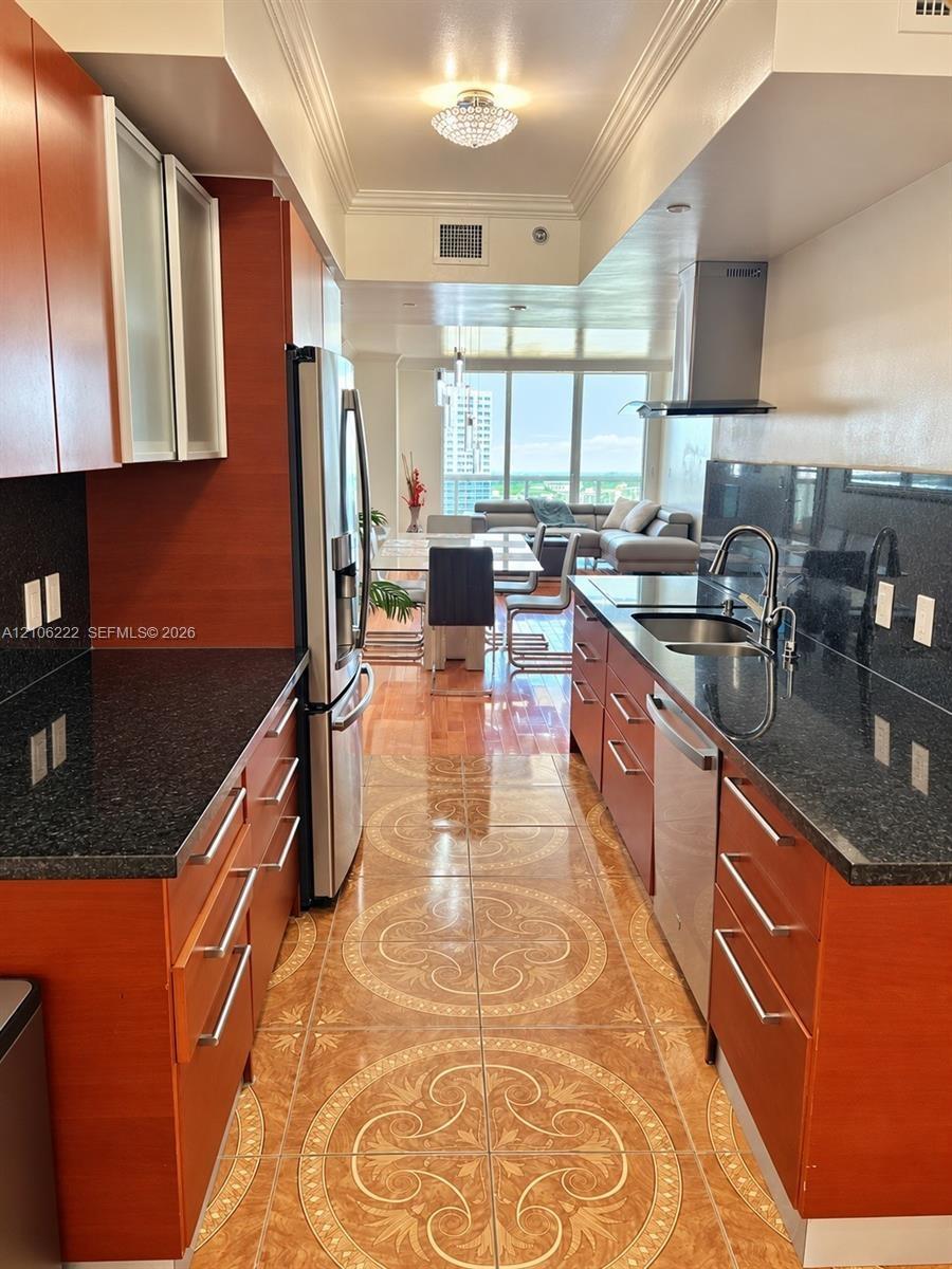Kitchen featuring rich wood-finish cabinetry, dark stone countertops, patterned ceramic tile flooring, stainless steel appliances, and a modern stainl
