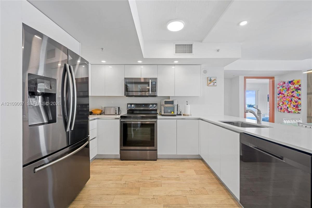 Kitchen featuring white flat-panel cabinetry, quartz countertops, stainless steel appliances, and wood-finish flooring